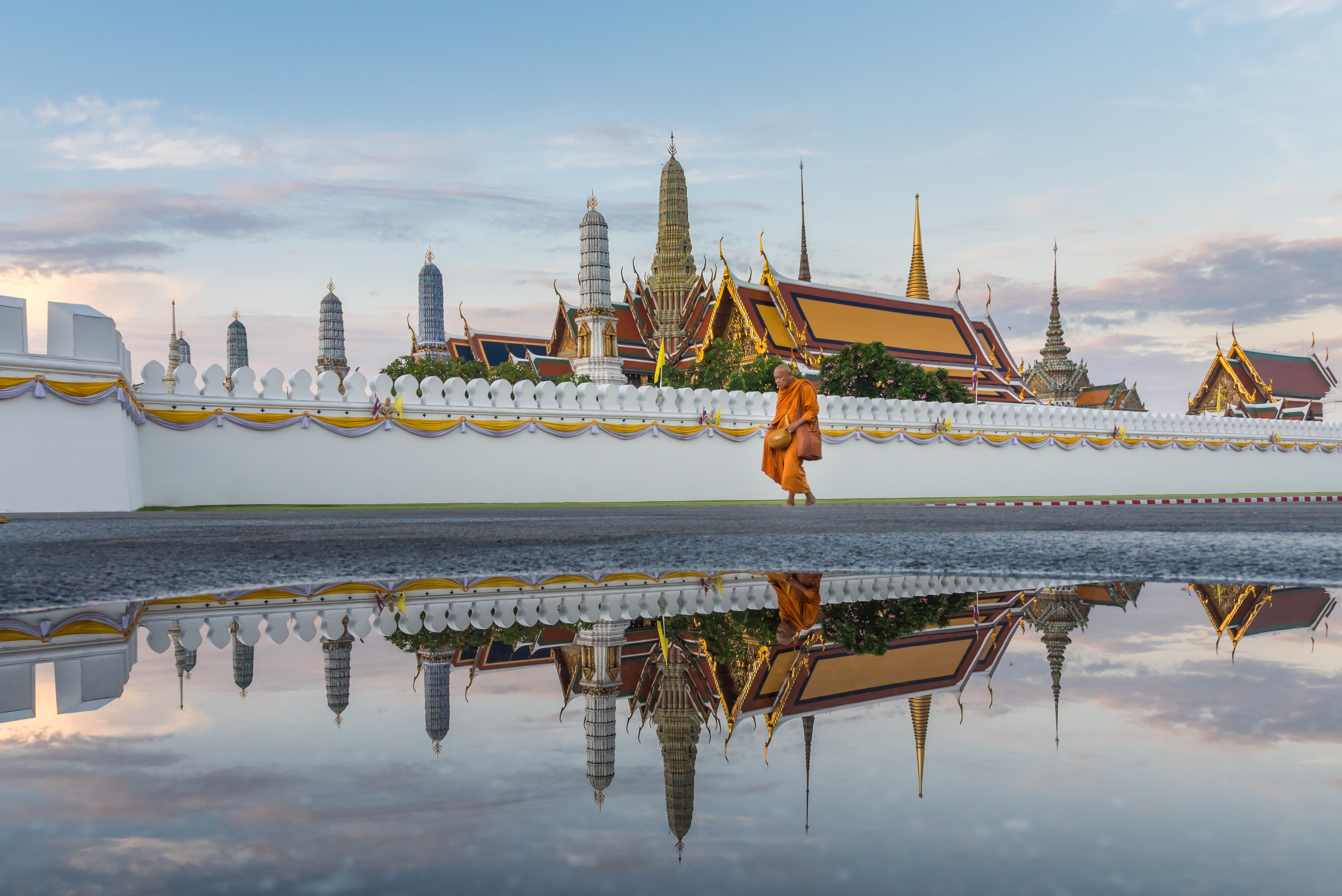 A monk walks in the morning after the rain in front of the Temple of the Emerald Buddha (Wat Phra Kaew), part of the Grand Palace in Bangkok, Thailand.